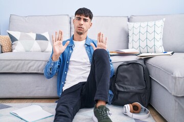 Young hispanic man sitting on the floor studying for university moving away hands palms showing...
