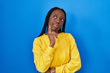 Beautiful black woman standing over blue background with hand on chin thinking about question, pensive expression. smiling with thoughtful face. doubt concept.
