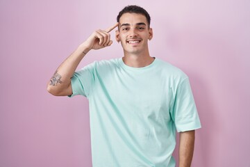 Handsome hispanic man standing over pink background smiling pointing to head with one finger, great idea or thought, good memory