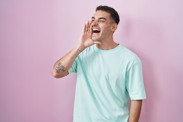 Handsome hispanic man standing over pink background shouting and screaming loud to side with hand on mouth. communication concept.