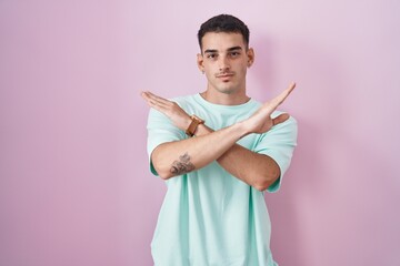 Handsome hispanic man standing over pink background rejection expression crossing arms doing negative sign, angry face