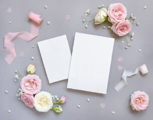 Obraz na płótnie Canvas Blank paper cards between pink roses and pink silk ribbons on grey top view, wedding mockup