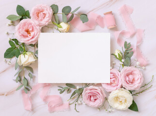 Blank paper card between pink roses and silk ribbons on marble top view, wedding mockup