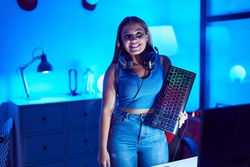 Young blonde woman playing video games with smartphone holding keyboard looking positive and happy standing and smiling with a confident smile showing teeth