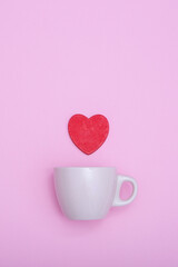 Coffee cup and red wooden heart on a pink background. The concept of Valentine's day, love, dating and wedding. Symbol of a romantic gift or marriage proposal. Copy space, minimalism, vertical photo.