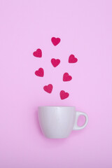 Coffee cup and wooden hearts on a pink background. The concept of Valentine's day, love, dating and wedding. Symbol of a romantic gift or marriage proposal. Vertical photo, minimalism.