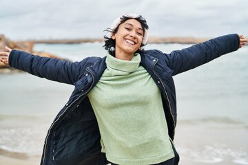 Young beautiful hispanic woman smiling confident standing with arms open at seaside