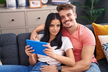 Man and woman couple using touchpad sitting on sofa at home