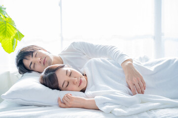 寝室のベッドで眠る若い夫婦-朝