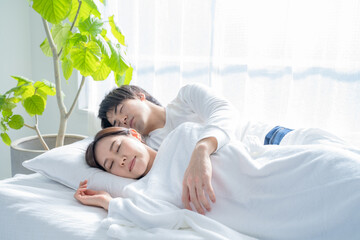 寝室のベッドで眠る若い夫婦-朝
