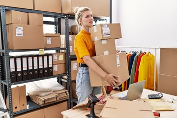 Young blonde woman working at small business ecommerce clueless and confused expression. doubt...