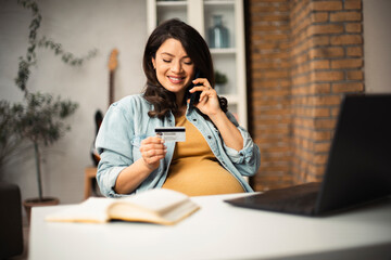 Pregnant woman shopping online at home. Happy woman with laptop and credit card.