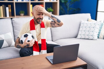 Hispanic man with tattoos watching football match hooligan holding ball on the laptop stressed and...