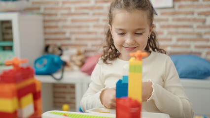 Adorable caucasian girl playing with construction blocks sitting on table at kindergarten