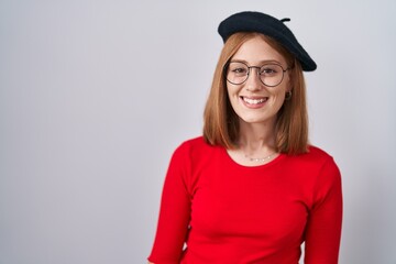 Young redhead woman standing wearing glasses and beret with a happy and cool smile on face. lucky person.