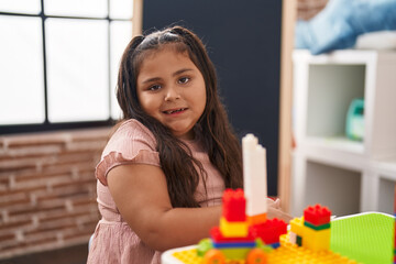 Plus size hispanic girl playing with construction blocks sitting on table at kindergarten