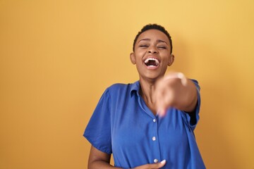African american woman standing over yellow background laughing at you, pointing finger to the camera with hand over body, shame expression
