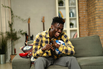 Young African man watching sport match on television and supporting his favorite team. Happy man enjoying victory, watching sports competition on tv..