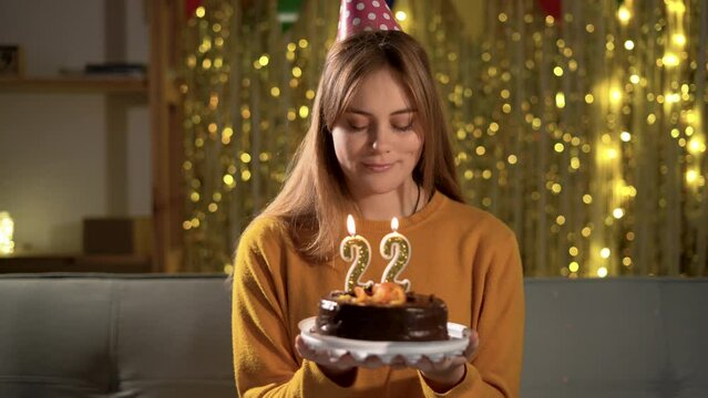 22th birthday. Young woman blowing candle twenty two on a birthday cake. Girl making a wish while holding a cake