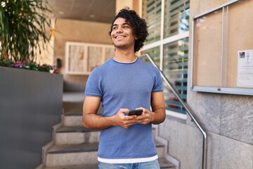 Young hispanic man smiling confident using smartphone at street