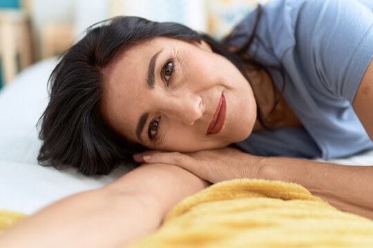 Middle age hispanic woman smiling confident lying on bed at bedroom
