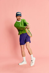 Portrait of young man in vintage sportive clothes playing tennis isolated over pink background. Student's hobby