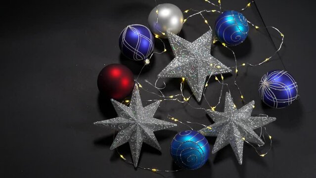 Beautiful Christmas decoration with colorful Christmas baubles and silver glittering stars and yellow led lights against black background. Movie shot December 15th, 2022, Zurich, Switzerland.