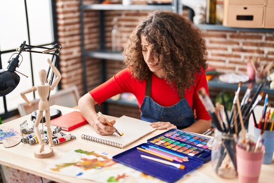 Young hispanic woman artist drawing on notebook at art studio