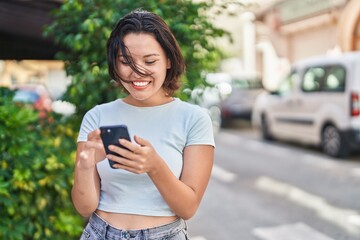 Young hispanic woman smiling confident using smartphone at street