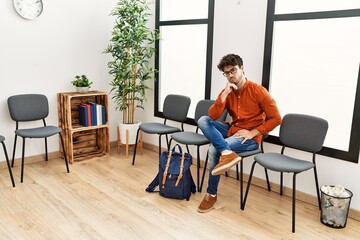 Young hispanic man boring sitting on chair at waiting room
