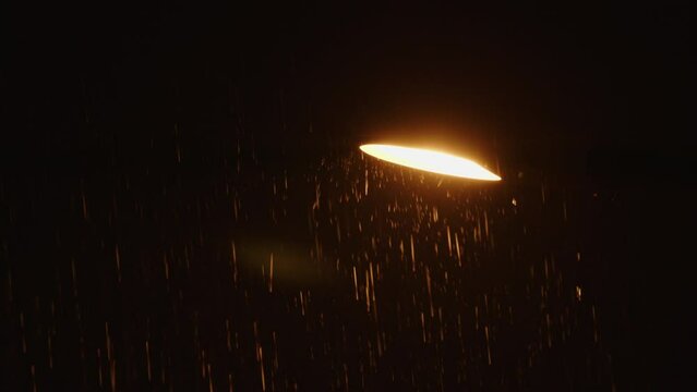 yellow street lamp in rain. Lantern over road shining yellow, 3000 kelvin, it raining hard, drops reflect light of bulb.