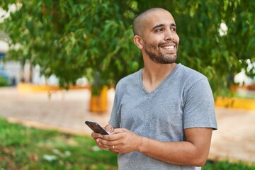 Naklejka na ściany i meble Young latin man smiling confident using smartphone at park