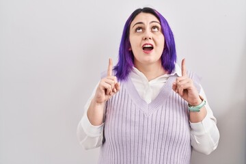 Obraz na płótnie Canvas Plus size woman wit purple hair standing over white background amazed and surprised looking up and pointing with fingers and raised arms.