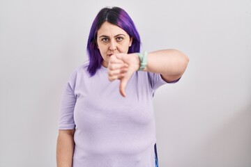 Plus size woman wit purple hair standing over isolated background looking unhappy and angry showing rejection and negative with thumbs down gesture. bad expression.