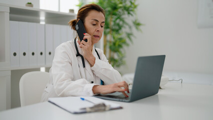 Middle age hispanic woman wearing doctor uniform talking on the smartphone at clinic
