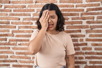 Fototapeta na wymiar Young hispanic woman standing over bricks wall yawning tired covering half face, eye and mouth with hand. face hurts in pain.