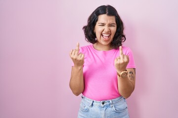 Obraz na płótnie Canvas Young hispanic woman standing over pink background showing middle finger doing fuck you bad expression, provocation and rude attitude. screaming excited