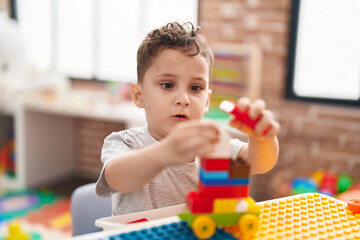 Adorable hispanic toddler playing with construction blocks sitting on table at kindergarten