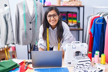 Young beautiful hispanic woman tailor smiling confident using laptop at clothing factory