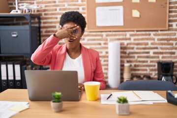 Young african american woman working at the office wearing glasses peeking in shock covering face and eyes with hand, looking through fingers afraid