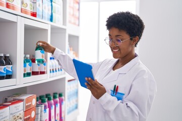 African american woman pharmacist using touchpad holding medication bottle at pharmacy