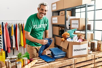 Middle age grey-haired man volunteer smiling confident folding jeans at charity center
