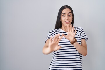 Young brunette woman wearing striped t shirt afraid and terrified with fear expression stop gesture with hands, shouting in shock. panic concept.