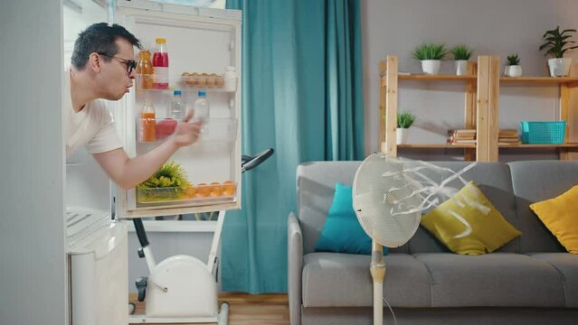 funny man suffering from a heat problem looks out of the refrigerator dissatisfied