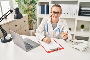 Young blonde woman wearing doctor uniform prescribe pills at clinic
