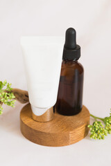 Obraz na płótnie Canvas Cream tube and glass bottle with serum white background with natural wood and fresh leaves