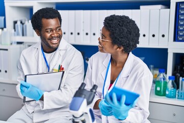 African american man and woman scientists using touchpad write on document at laboratory