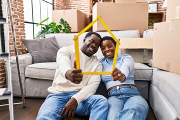 Man and woman couple holding house project sitting on floor at new home