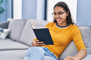 Naklejka premium Young african american woman reading book sitting on sofa at home