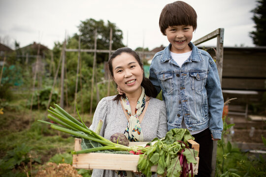 Portrait happy mother and son with harvested vegetables in garden